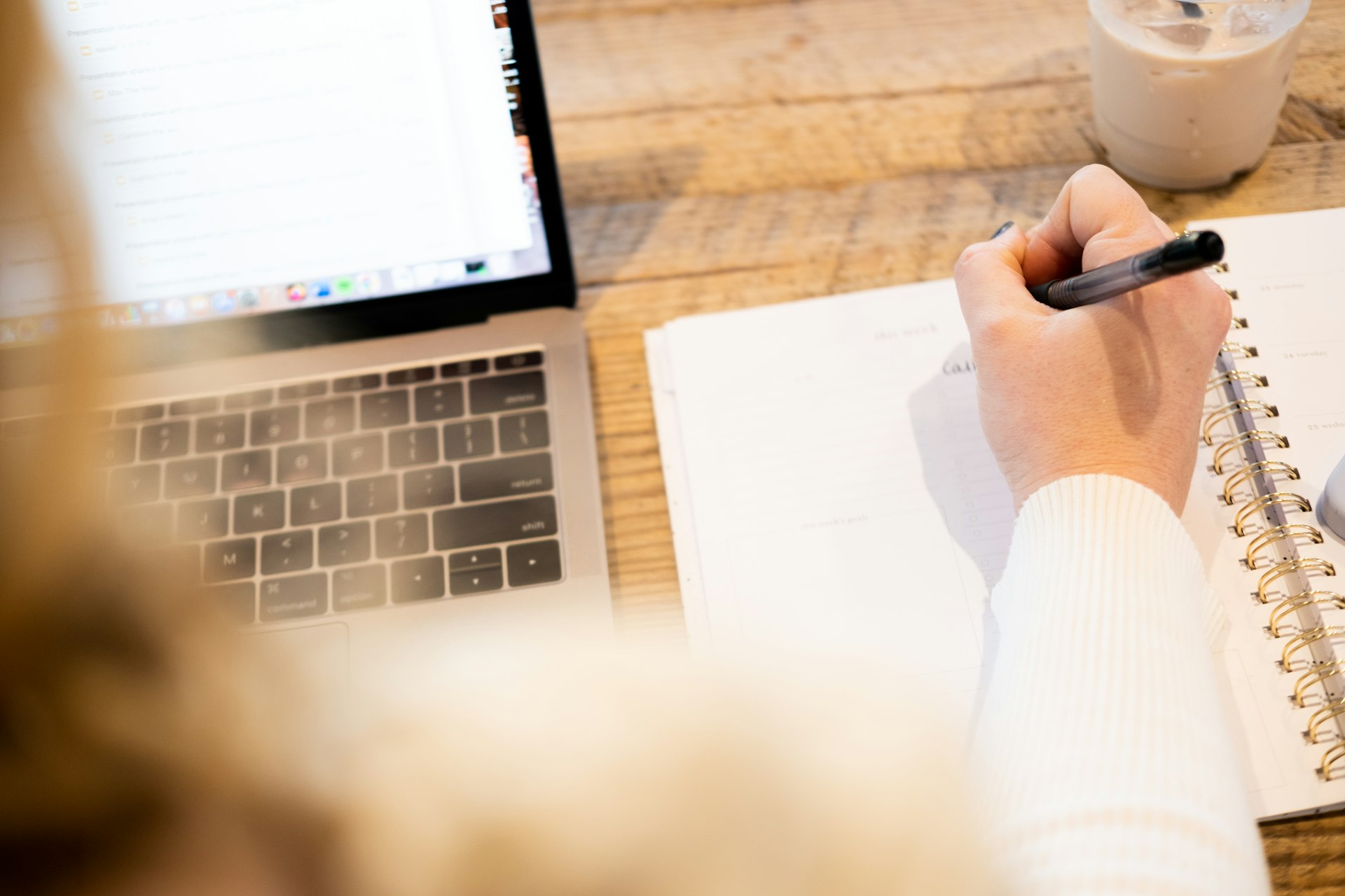 a person writing on a notebook next to a laptop